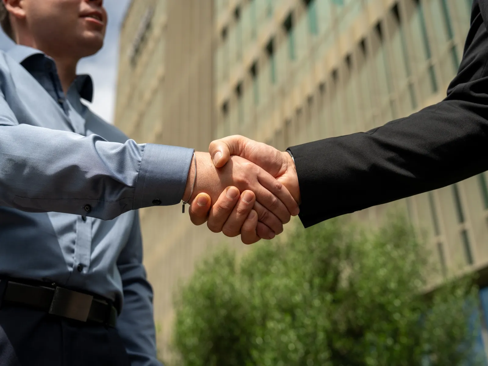 Peer Grewolls and Joao Pedro Madeira Amorim shaking hands in front of an office building.
